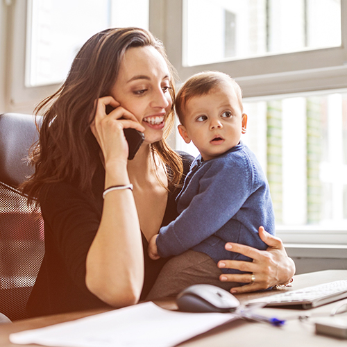 mother on cellphone holding baby at her desk