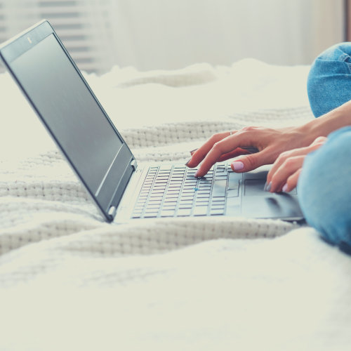 laptop on bed with someone hands typing in